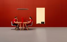 two people sitting at a table in front of a red wall with a light hanging from the ceiling