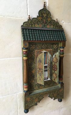 an ornate wooden clock mounted to the side of a wall with a book shelf below it