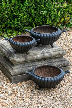 three black pots sitting on top of each other in the middle of gravel covered ground