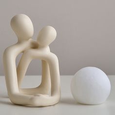 two white ceramic figurines sitting next to each other on a table with a ball in the foreground