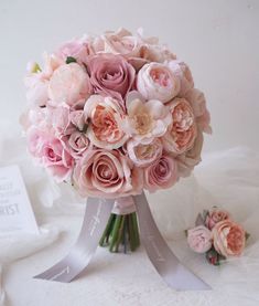 a bridal bouquet with pink roses on a white tablecloth next to a card