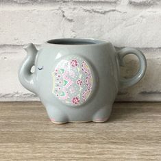 an elephant shaped ceramic cup sitting on top of a wooden table next to a brick wall