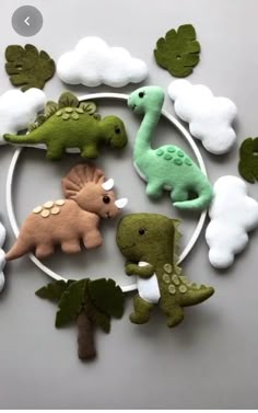 felt dinosaurs are arranged in a circle with clouds and leaves on the top one is green, white, and brown