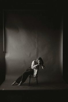 a black and white photo of a woman sitting on a chair with her head in her hands