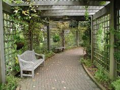 a white bench sitting under a pergoline covered arbor in the middle of a park