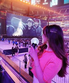 a woman holding a white frisbee in front of a large screen at an arena