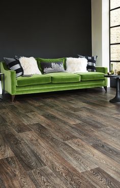 a living room with wood flooring and green couch in the center, along with black walls