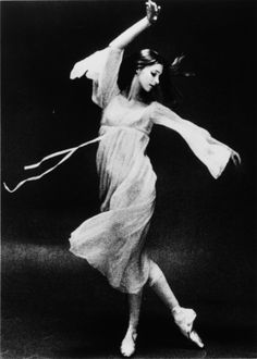 a woman in a white dress is dancing with a long ribbon around her neck and arm