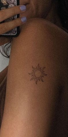 a woman with a small sun tattoo on her arm holding a cell phone and taking a selfie