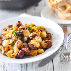 a white plate topped with potatoes and meat next to a fork on a wooden table