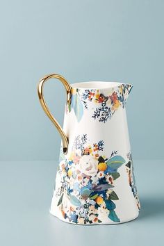 a white and blue flowered vase with gold handles on a light blue table top