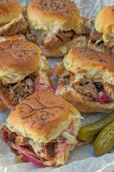 sandwiches with meat, cheese and pickles sitting on wax paper