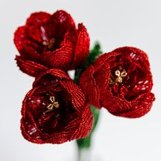 three red flowers in a glass vase on a white tableclothed surface with beading