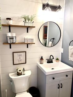 a white toilet sitting next to a sink in a bathroom under a mirror and shelves