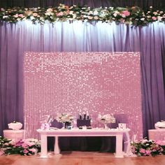 a table with flowers and candles on it in front of a purple backdrop that has sequins