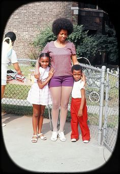 a woman and two children standing in front of a fence