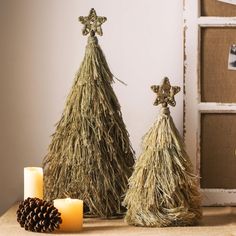 two christmas trees made out of hay and pine cones with candles on the table next to them