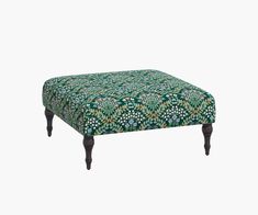 a footstool that is covered in a green and white floral print with wooden legs