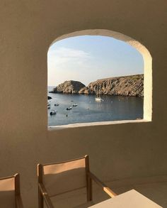 two chairs sitting in front of an open window overlooking the ocean with boats on the water