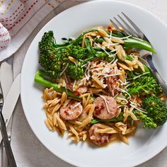 a white plate topped with pasta and broccoli next to a knife and fork