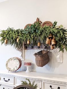 a white mantle topped with lots of greenery and bells on it's hooks