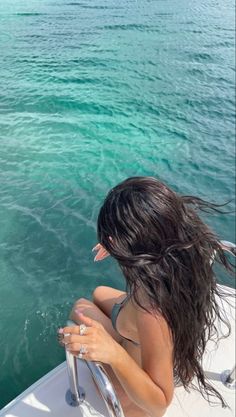 a woman sitting on the bow of a boat in clear blue water with her hair blowing back