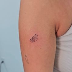 a woman's arm with a small piece of fruit tattoo on the left shoulder