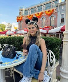 a woman sitting at a table with mickey mouse ears on her head, holding an ice cream cone