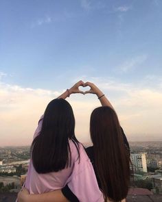 two girls making a heart shape with their hands in the air over a cityscape