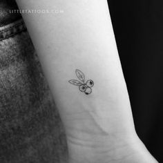 a small black and white tattoo of a bee on the left inner arm, with an olive in it's center