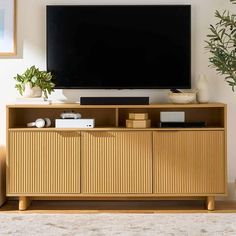 a flat screen tv sitting on top of a wooden entertainment center next to a potted plant