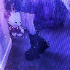 a person in black boots is standing near a wall with a hello kitty figure on it