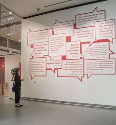 a woman standing in front of a white wall with lots of red words on it