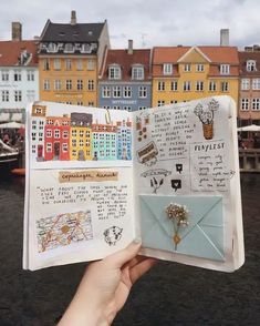 someone is holding up an open book with pictures and writing on it in front of some buildings