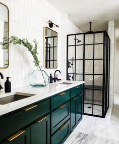 a bathroom with green cabinetry and marble counter tops, along with a white tiled wall