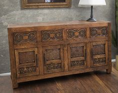 an old wooden sideboard with carvings on it and a lamp next to it in front of a painting