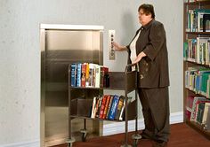 a man standing in front of a book shelf with a machine on it's side