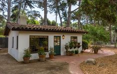 a small white house with potted plants on the front porch and door, surrounded by trees