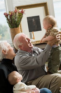 an older man holding a baby up to his face while sitting on a couch with two other people