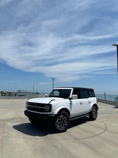 a white land rover parked on top of a parking lot next to the ocean with blue skies in the background