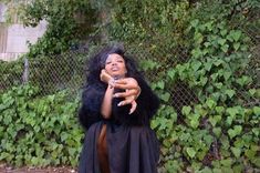 a woman dressed in black holding a cell phone up to her ear and pointing at the camera