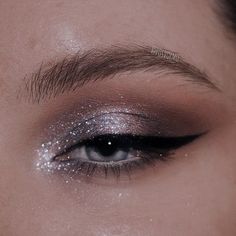 a woman's eye with silver glitter on her eyeshade and eyebrows, looking down at the camera