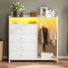 a white dresser with yellow drawers and clothes hanging on the top shelf next to it