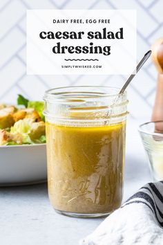 a glass jar filled with caesar salad dressing next to a bowl of salad and a spoon