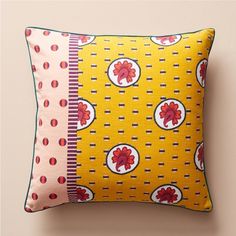 a yellow pillow with red flowers and circles on the front, sitting against a beige wall