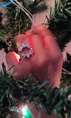 a woman's hand holding an engagement ring on top of a christmas tree branch