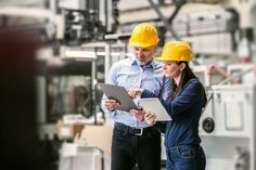 two people in hardhats looking at something on a clipboard while standing next to each other