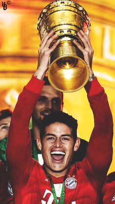 a soccer player holding up a trophy in front of his head and other people behind him