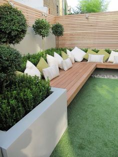 a wooden bench sitting on top of a grass covered field next to a tree and shrubbery