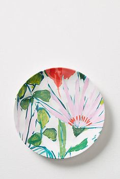 a white plate with pink and green flowers painted on the side, sitting on a wall